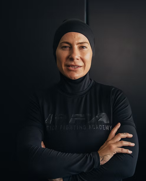 Person wearing a black outfit with 'Fighting Academy' text against a dark background